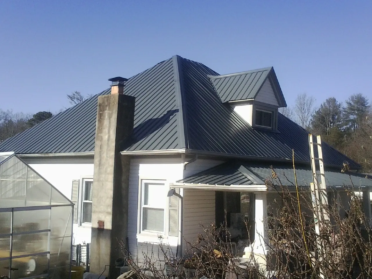 Dark blue standing seam metal roof on a white farmhouse with dormer — Slate & Tile Roof Repair by Roofing Brothers in Pinetops