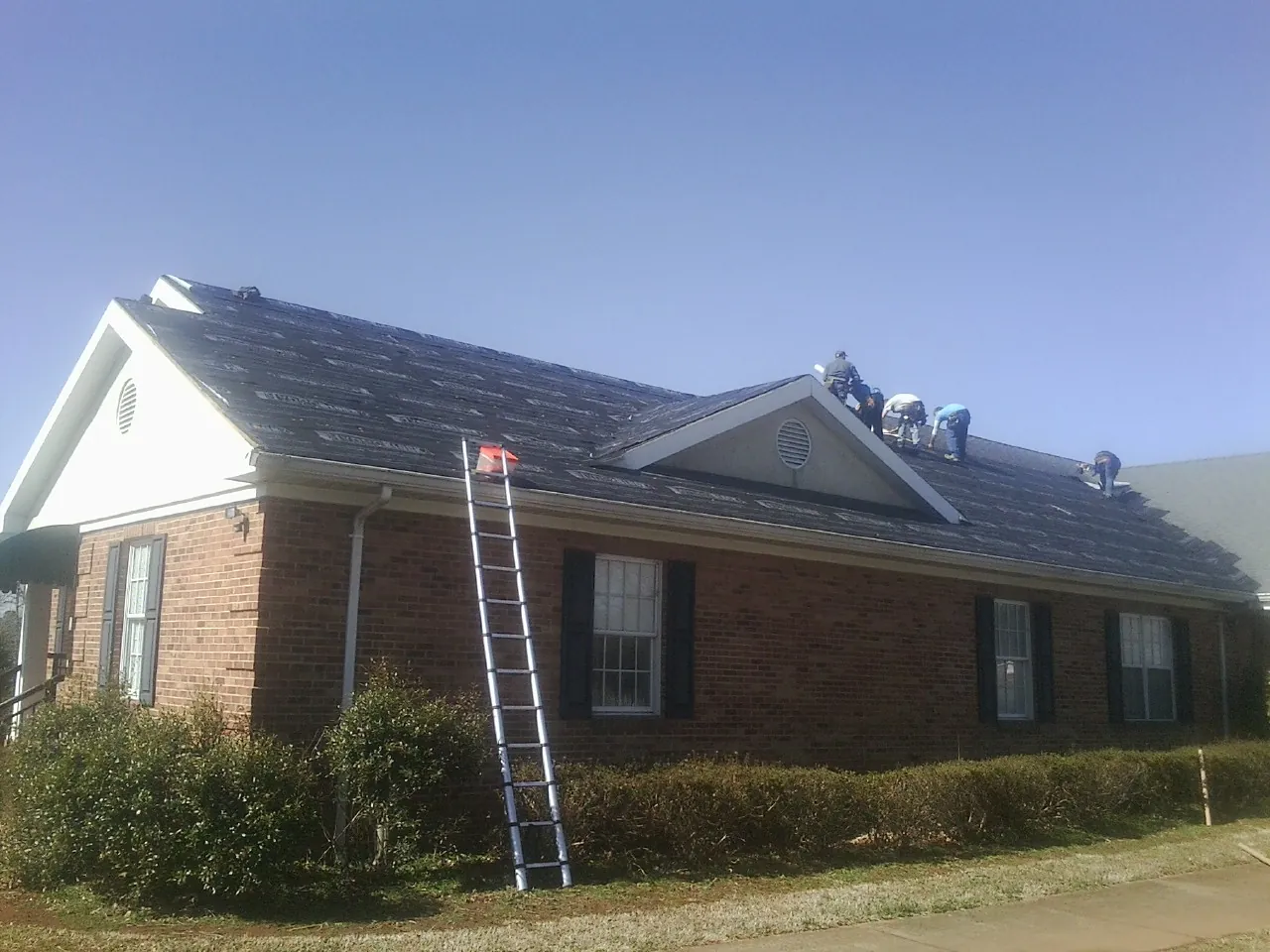 Crew tearing shingles off a brick ranch roof with a ladder set — Metal Roof Repair work by our crew in Pinetops