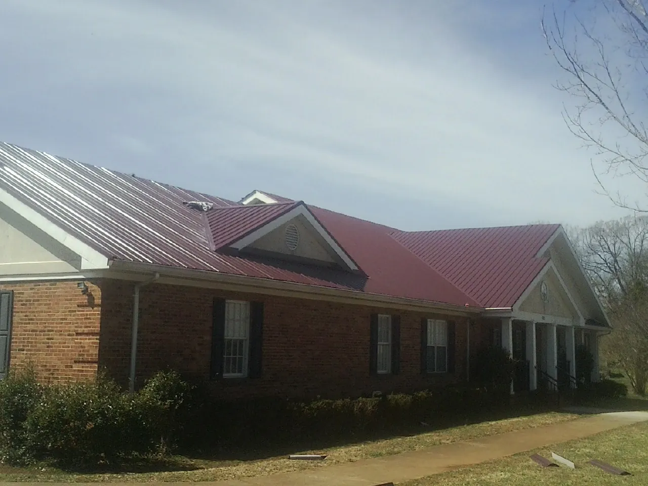 Red metal roof with gabled entries on a long brick building, from a Hail Damage Roof Repair job in Pinetops