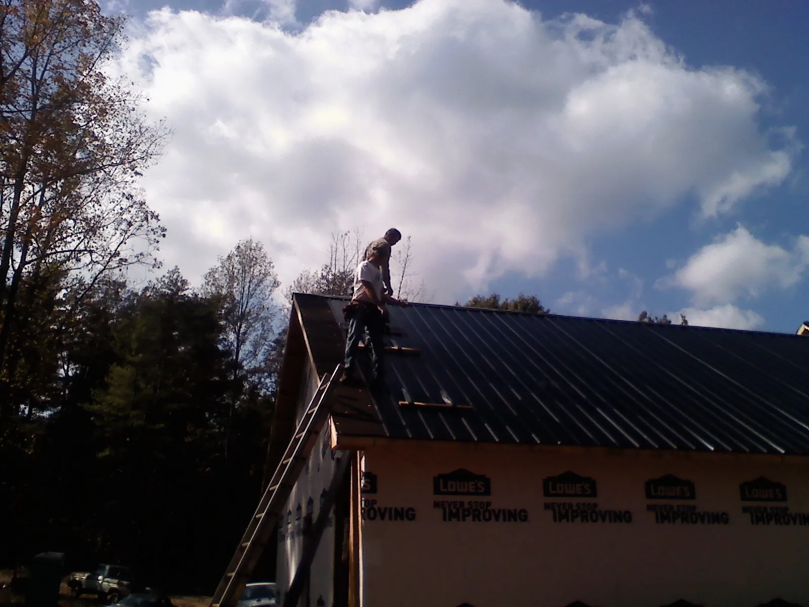 Roofer fastening dark metal panels high against a cloudy sky, from a Roof Inspection job in Pinetops