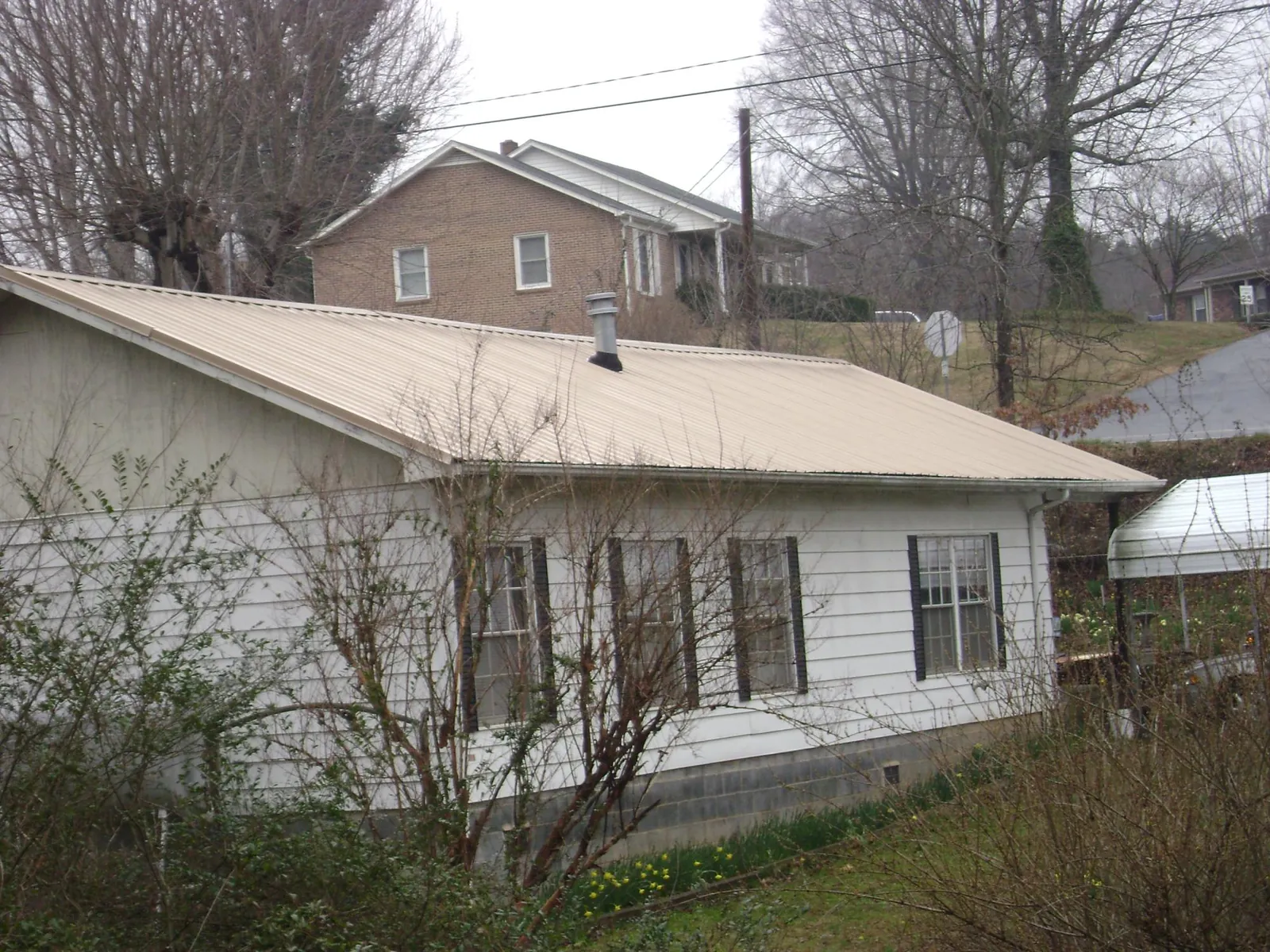 Tan metal roof on a white sided house set into a hillside — Commercial Roofing by Roofing Brothers in Pinetops