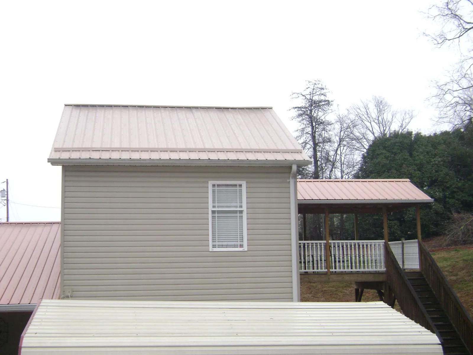 Tan metal roofs on a two story addition and attached porch, from a Roof Replacement job in Pinetops